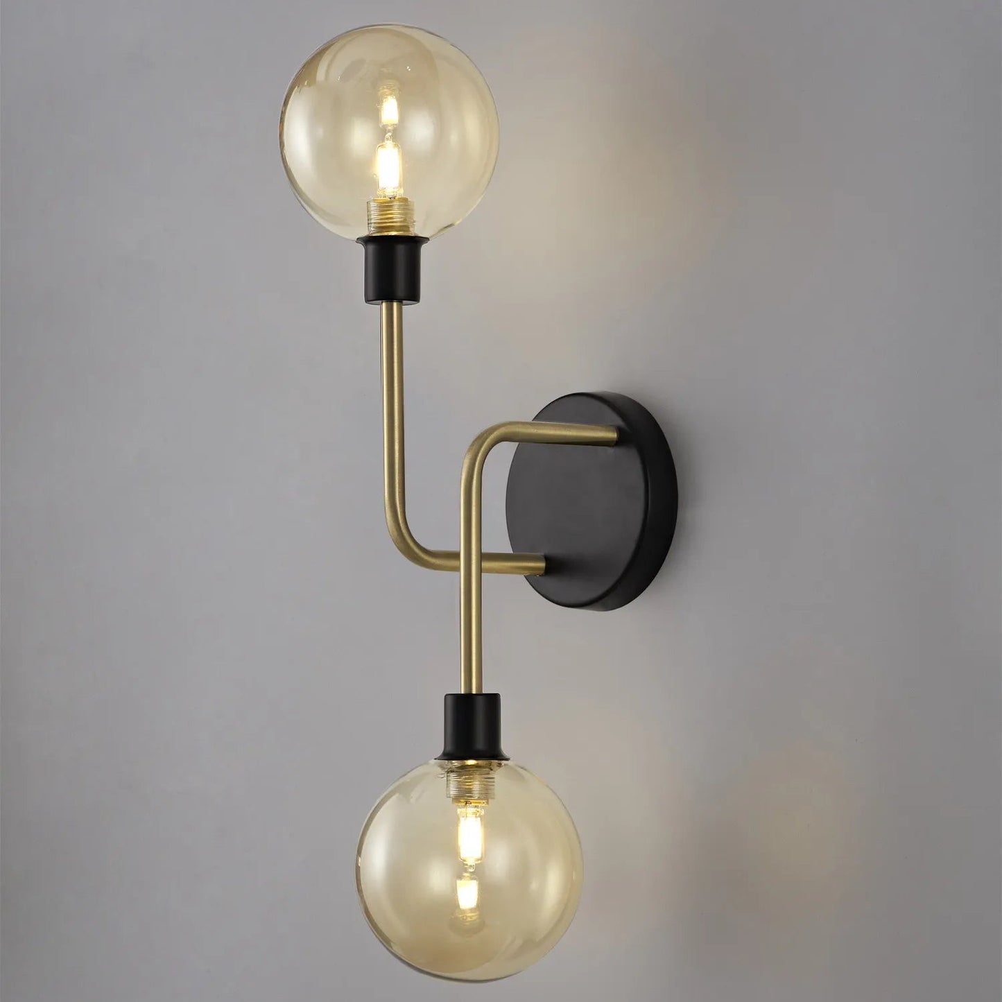 A wall-mounted light fixture with matt black frames and antique brass accents, featuring globe glass shades.