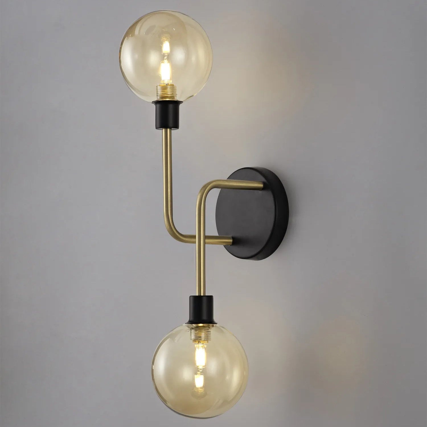 A wall-mounted light fixture with matt black frames and antique brass accents, featuring globe glass shades.